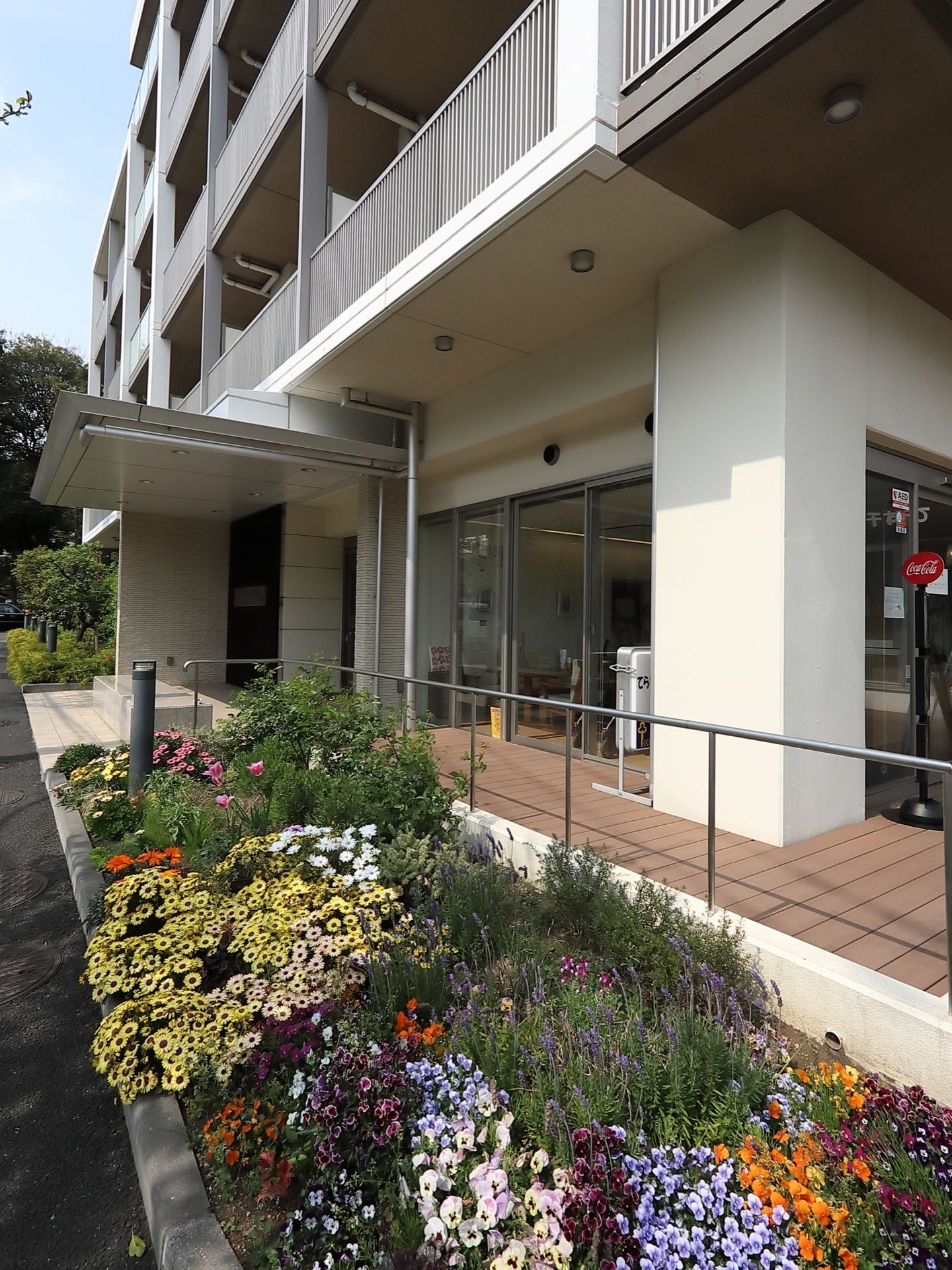 施設の玄関まで緩やかなスロープが続き、ステンレス製の手すりが取りつけられている。スロープの前には花壇がある。