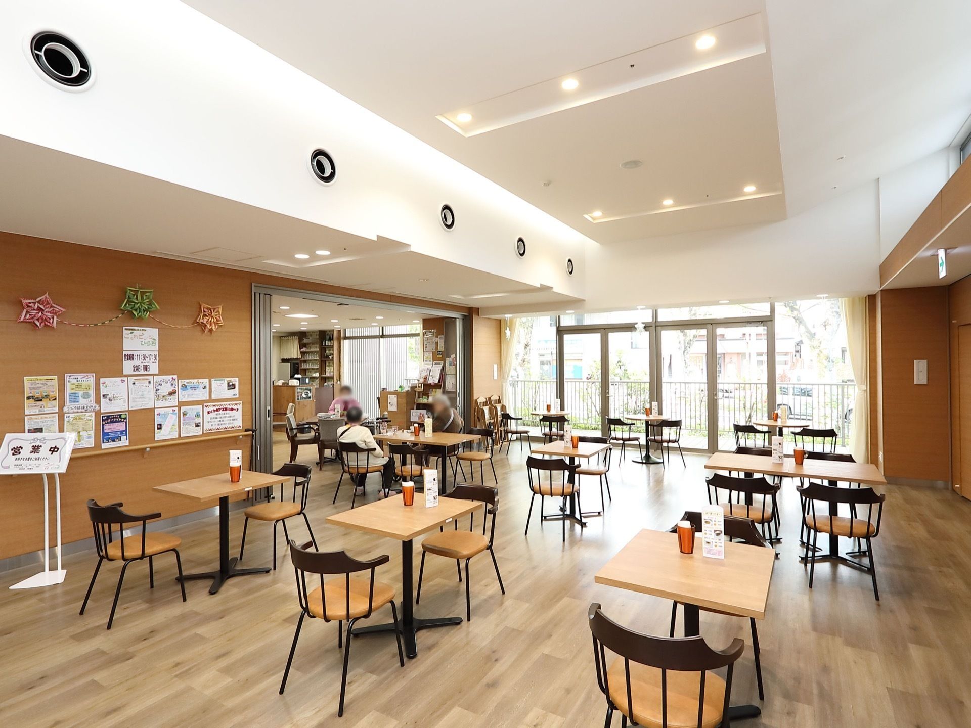 白とブラウンを基調とした、明るく落ち着きのある食堂の様子。２人用と４人用のテーブルセットが間隔を空けて配置されている。