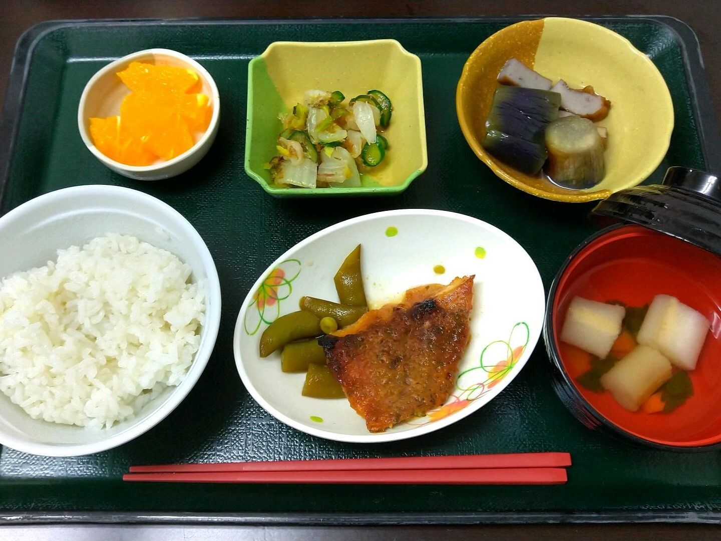 魚の唐揚げや汁物、キュウリの酢の物、野菜の煮つけ、白いご飯にフルーツが添えられ散る。