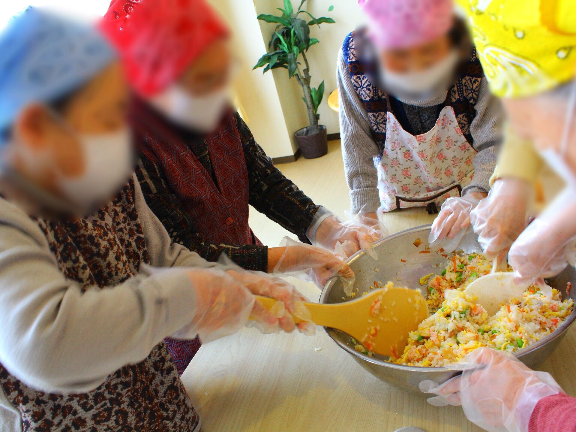 大きなしゃもじをもってすし飯を混ぜている女性と大きなボールを支えている女性たち。それぞれバンダナを頭に巻いている。