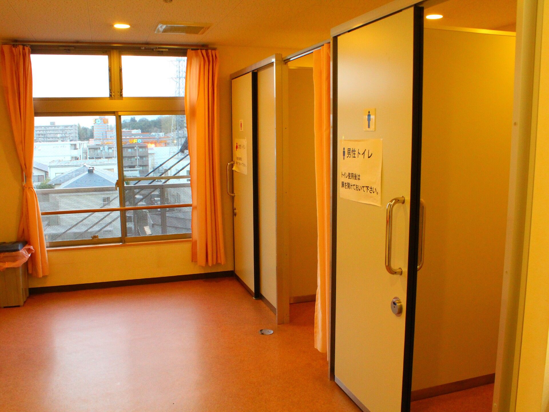 大きな窓が付いたトイレ。手前には男性マークが付いたトイレ、奥には女性マークが付いたトイレがあり、カーテンが付いている。