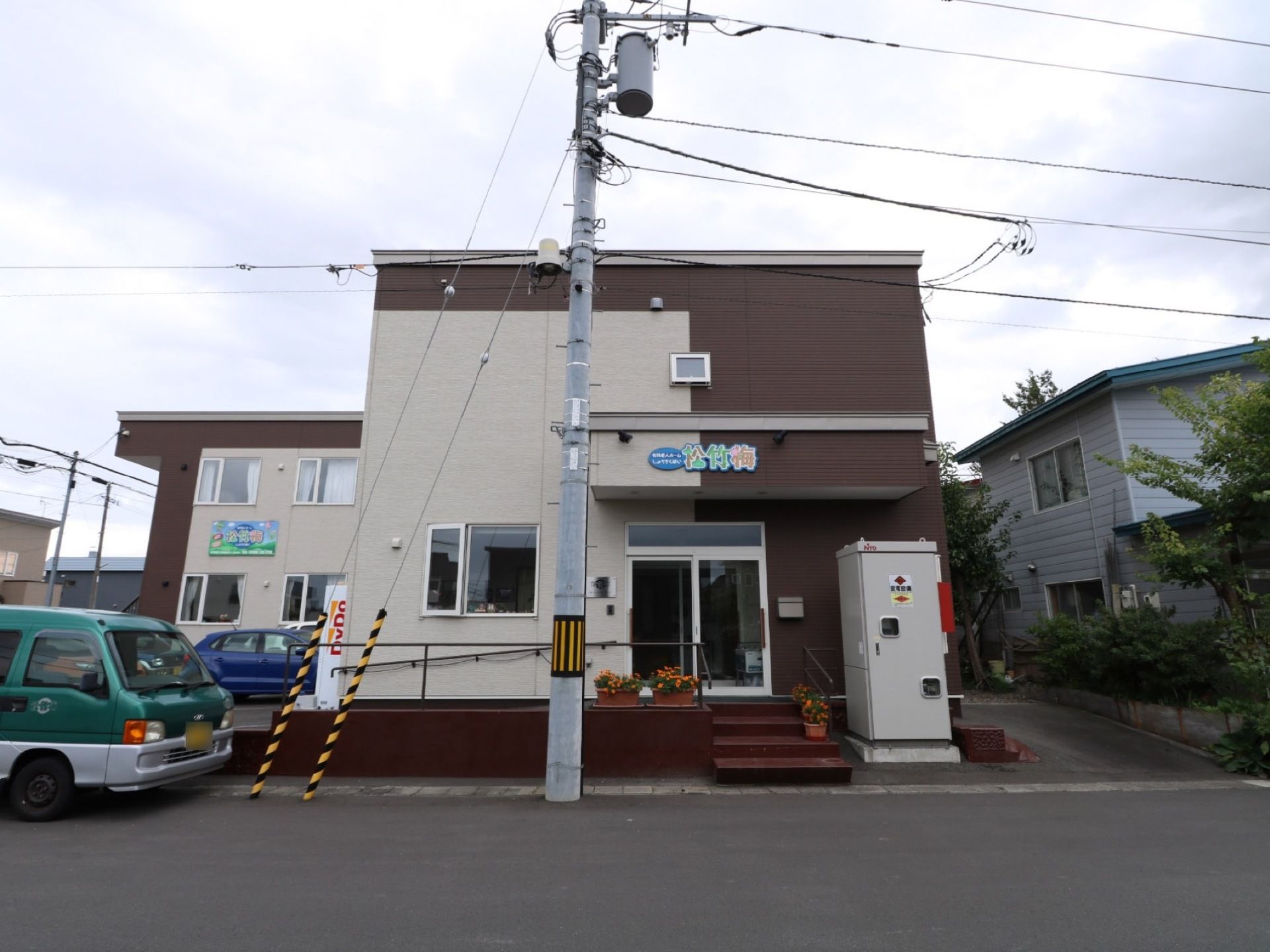白とブラウンのツートーンカラーで2階建ての施設である。L字型の建物で駐車場とスロープを完備している。