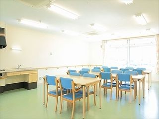 水色の椅子と四人掛けテーブルが複数組並んでいる施設内のリビングスペース