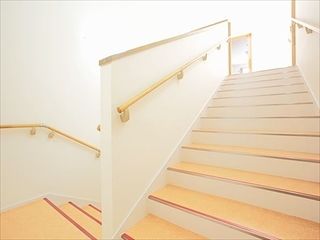 上から下まで手すりがついた施設内の階段の様子。幅が広いすべり止め付きの階段
