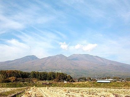 奥のほうに背の高い山、手前に畑が広がる景色の写真。秋晴れのような雰囲気