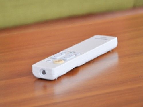 シンプルな白い照明のリモコン。薄いブルーやオレンジのボタンが付いていて、木製のテーブルの上に無造作に置かれている。