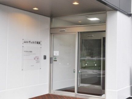 自動ドアが設置されたエントランスには段差がなく、風除室が付いている。外壁には住宅名が黒い文字で刻まれた透明なガラスのプレートが設置されている。