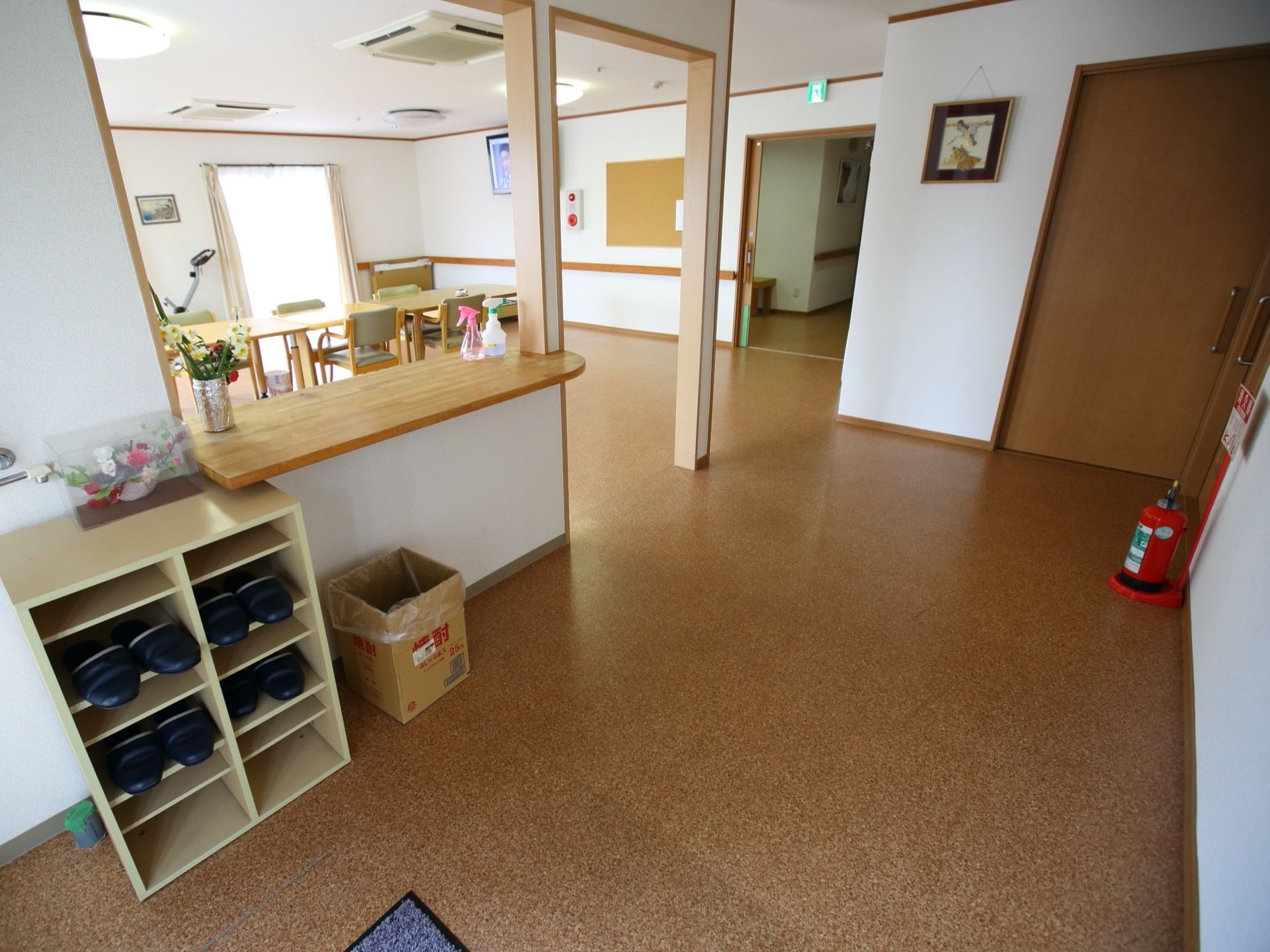 スリッパが収納された棚があり、その上にケースに入った花が飾られている。廊下の角に消火器が１台設置されている。