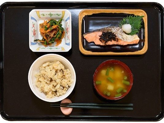 ご飯と魚のメイン野菜のおかずとみそ汁が並べられている昼食メニュー例