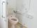 ふたのない便座が付いたトイレはスペースが広く、壁にはオレンジの呼び出しボタンと手すりが付いている。