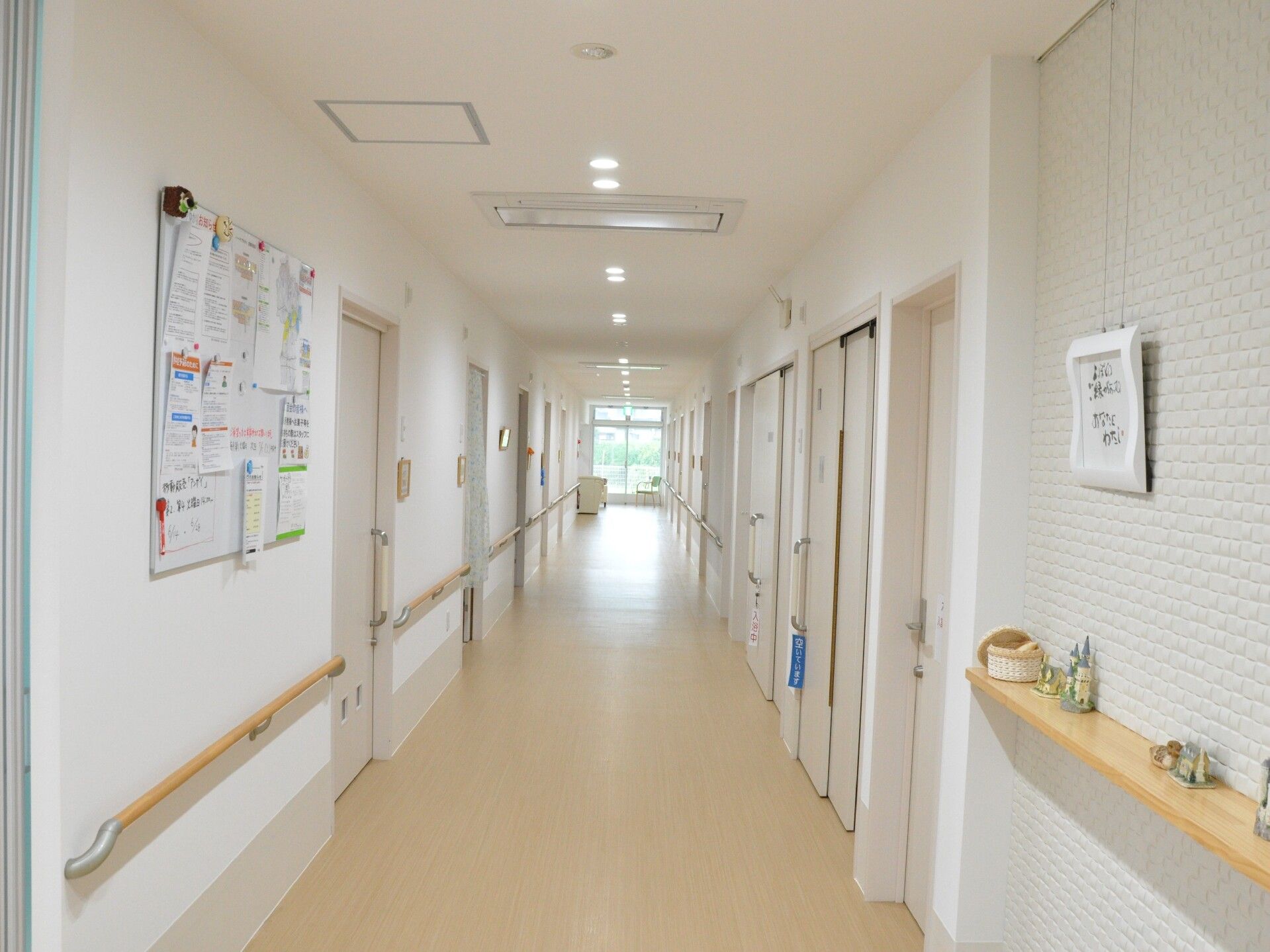 両サイドに手すりが付いたまっすぐな廊下。突き当りには窓があり、両サイドに居室のドアが並んでいる。