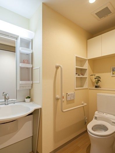 手前に洗面台がついている手すり付きのトイレの様子。やわらかい雰囲気の照明