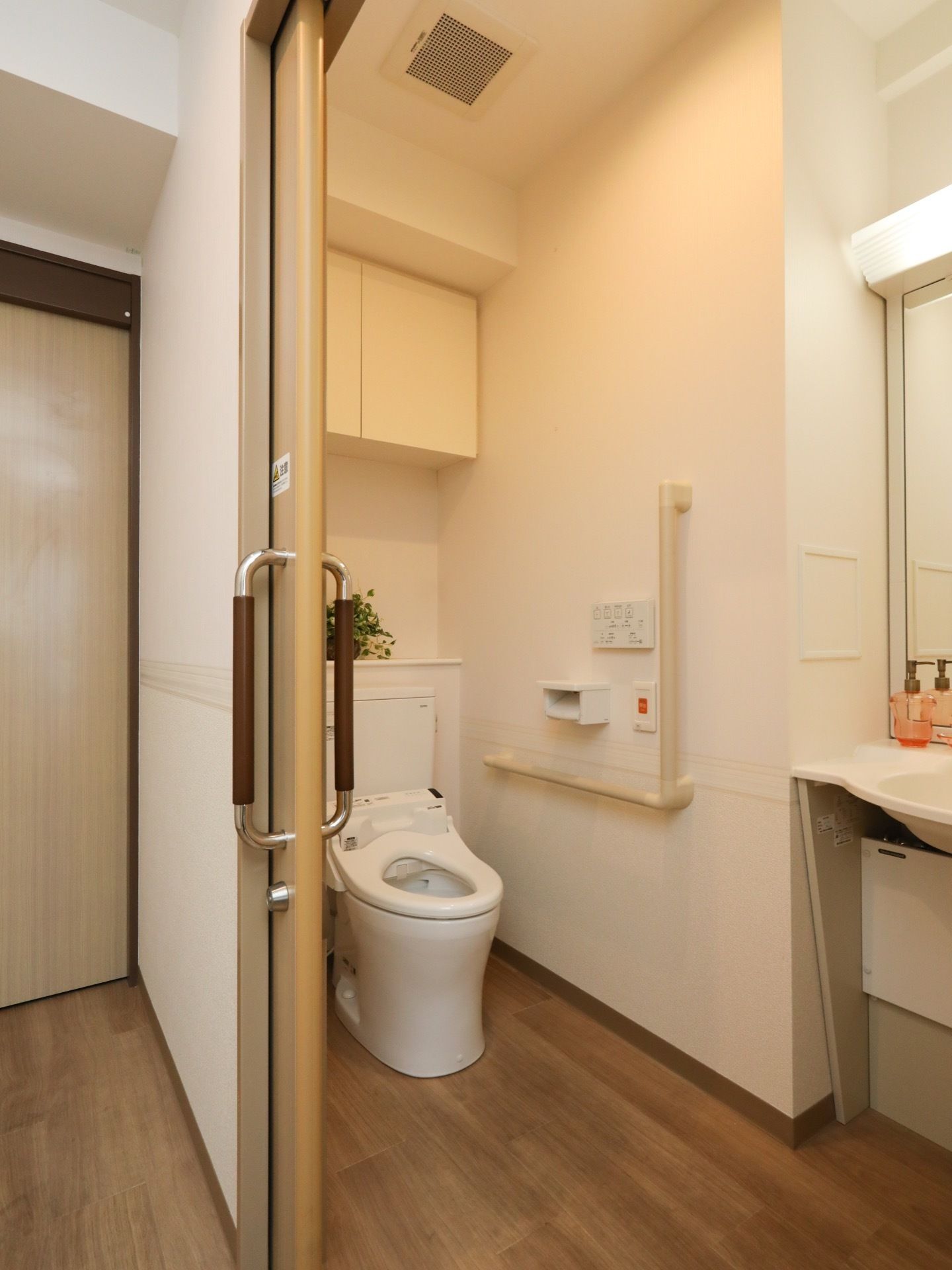 居室に広々とした洋式トイレが完備されている。扉は引き戸式で開口部が広い。壁側に手すりやナースコールが設置されている。