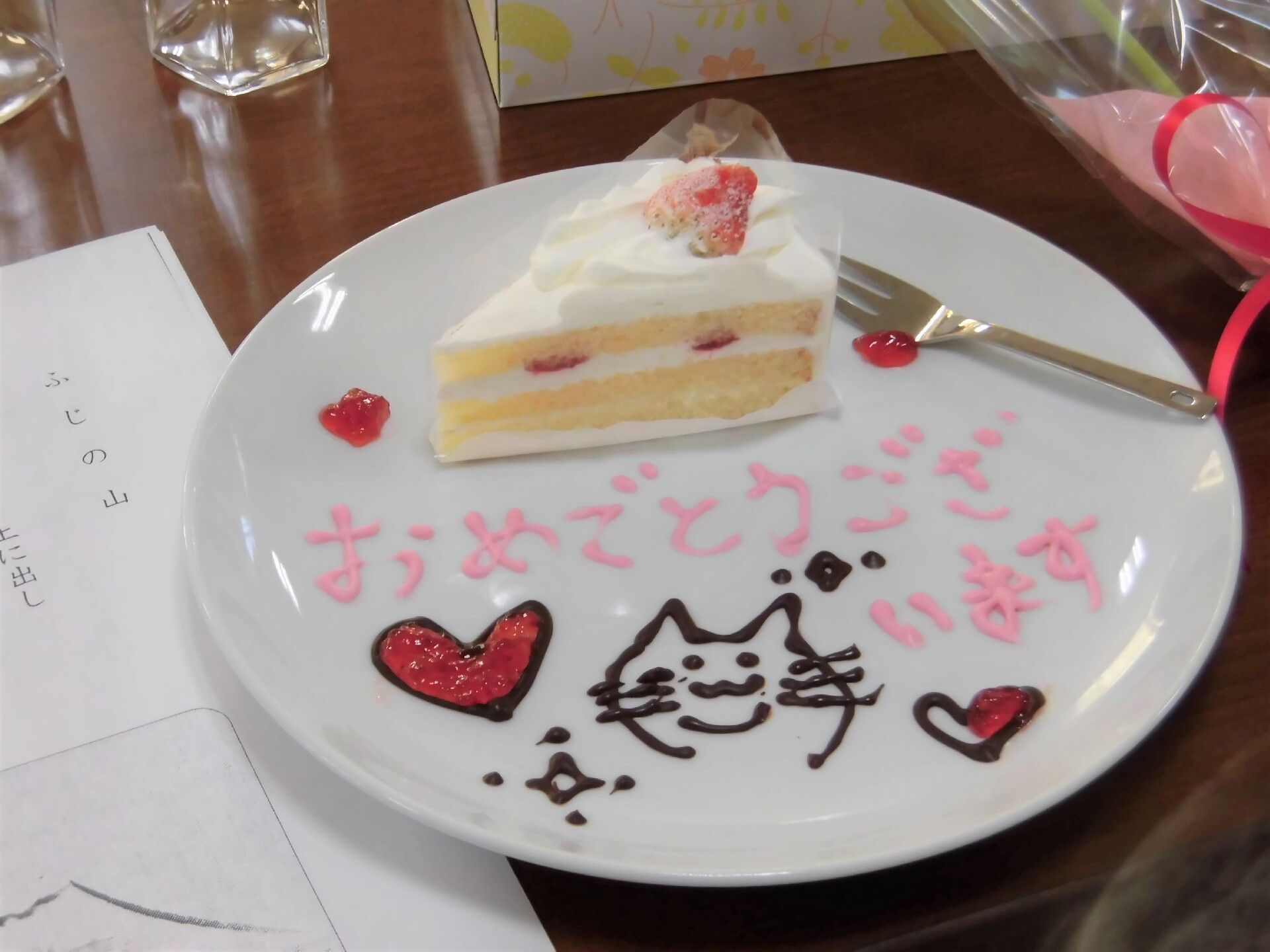 ショートケーキが乗った白いプレートには、チョコペンで猫のイラストやハート、「おめでとうございます」と書かれている。