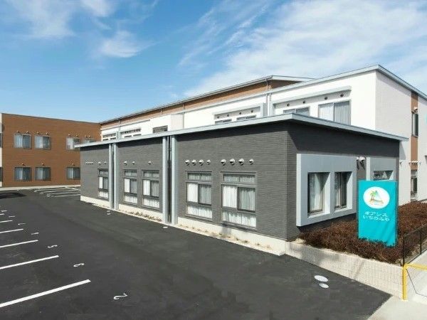 白とグレーの建物が手前に、奥には茶色の建物があり、駐車スペースも広い。