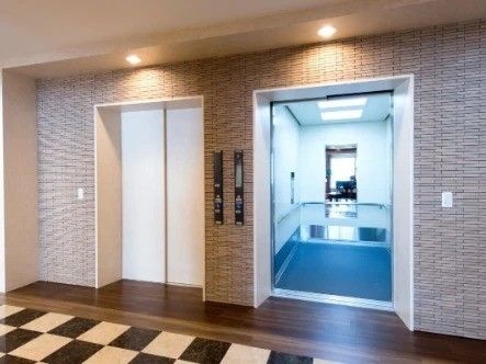 レンガ調の壁紙がおしゃれな雰囲気のエレベータースペース。大きなエレベーターが二つ並んでいる。