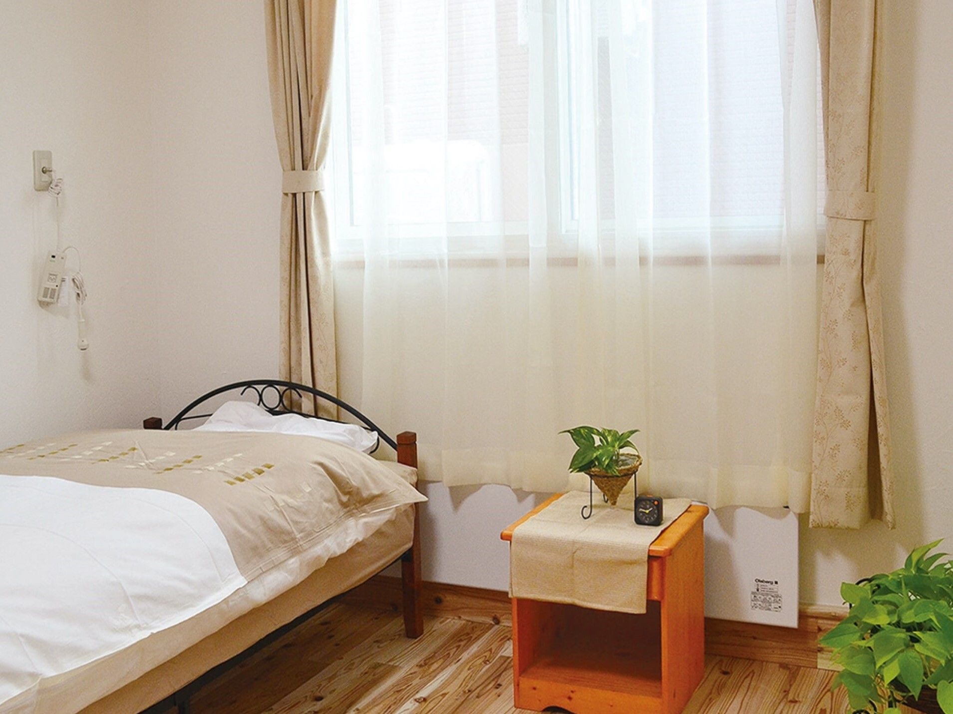 カーディガンを着た車いすの高齢女性が誰かに向かって手を振っている。そばにはエプロンを付けた若い女性スタッフが付き添っている。