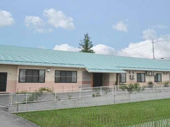 目の前に田んぼがある平屋建ての建物の玄関には屋根があり、敷地内には広い駐車場がある。