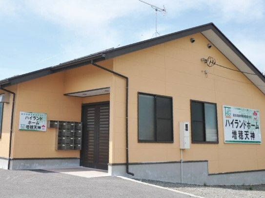 平屋建ての建物は日当たりのいい場所に建っている。外壁はベージュで三角屋根が付いている。