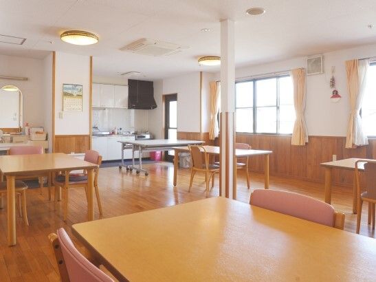木製のダイニングテーブルセットが複数置かれ、大きなキッチンが付いた食堂。