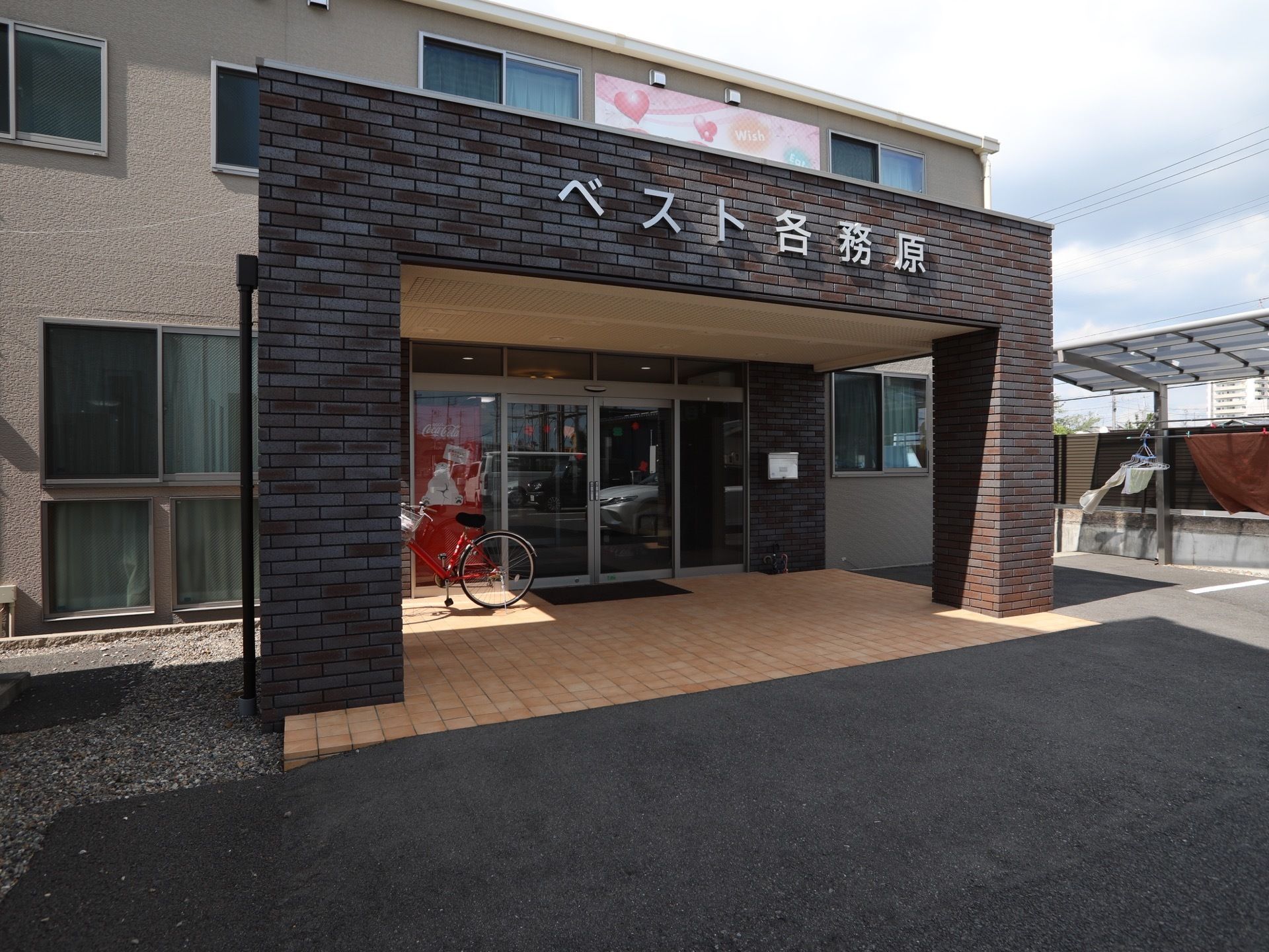 玄関は、ガラス張りのドアを採用している。前方に、側面がレンガ調の大きな屋根を設置している。上部に大きく施設名を表示している。