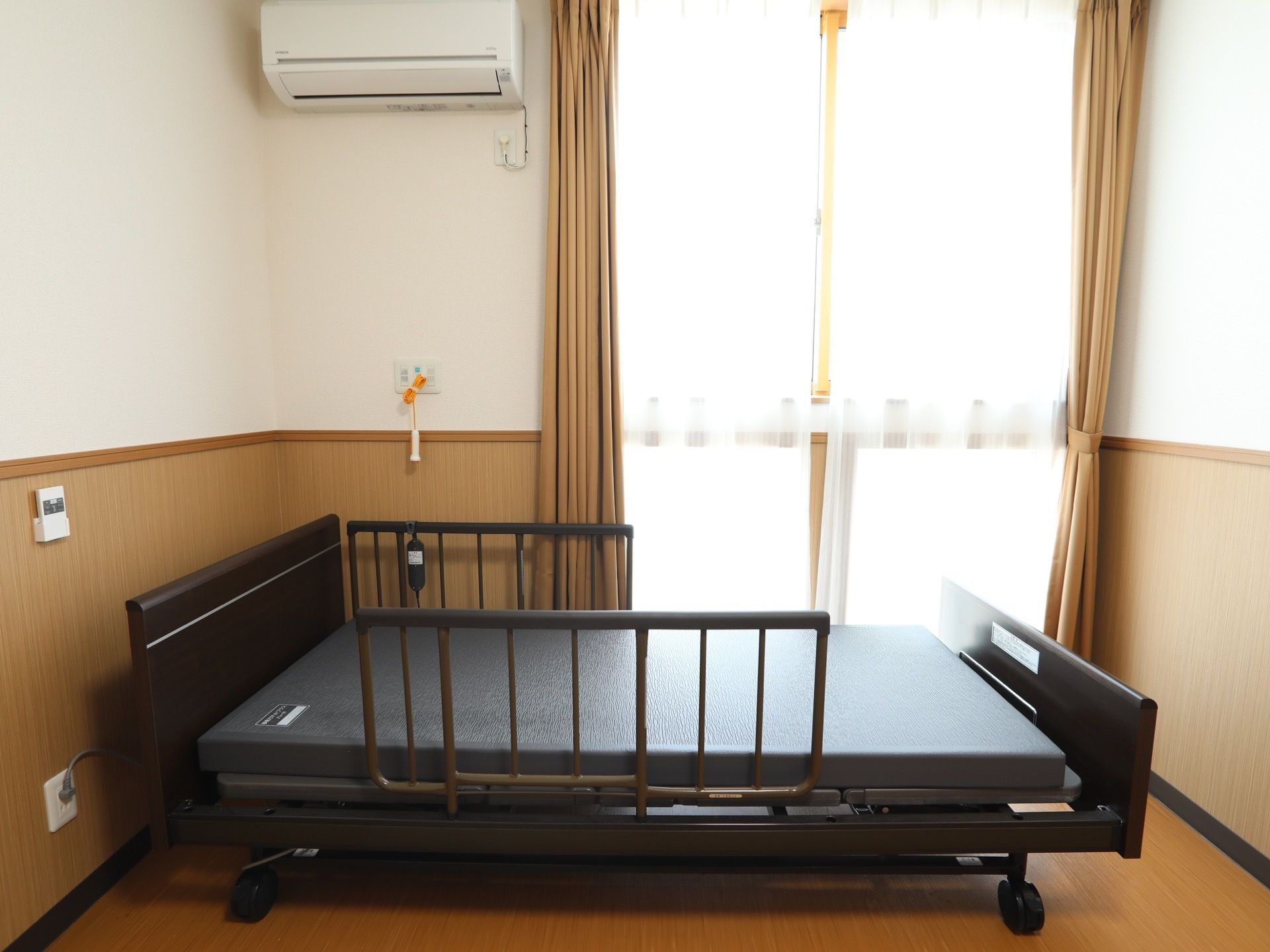 居室には、大きなガラス戸があり、傍に介護用ベッドを置いている。その横側にナースコールを取付け、天井下にエアコンを設置している。