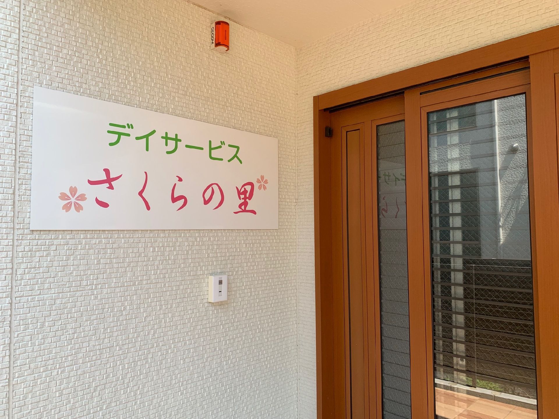 デイサービスの玄関。施設名の書かれた看板がある。扉は引き戸になっている。