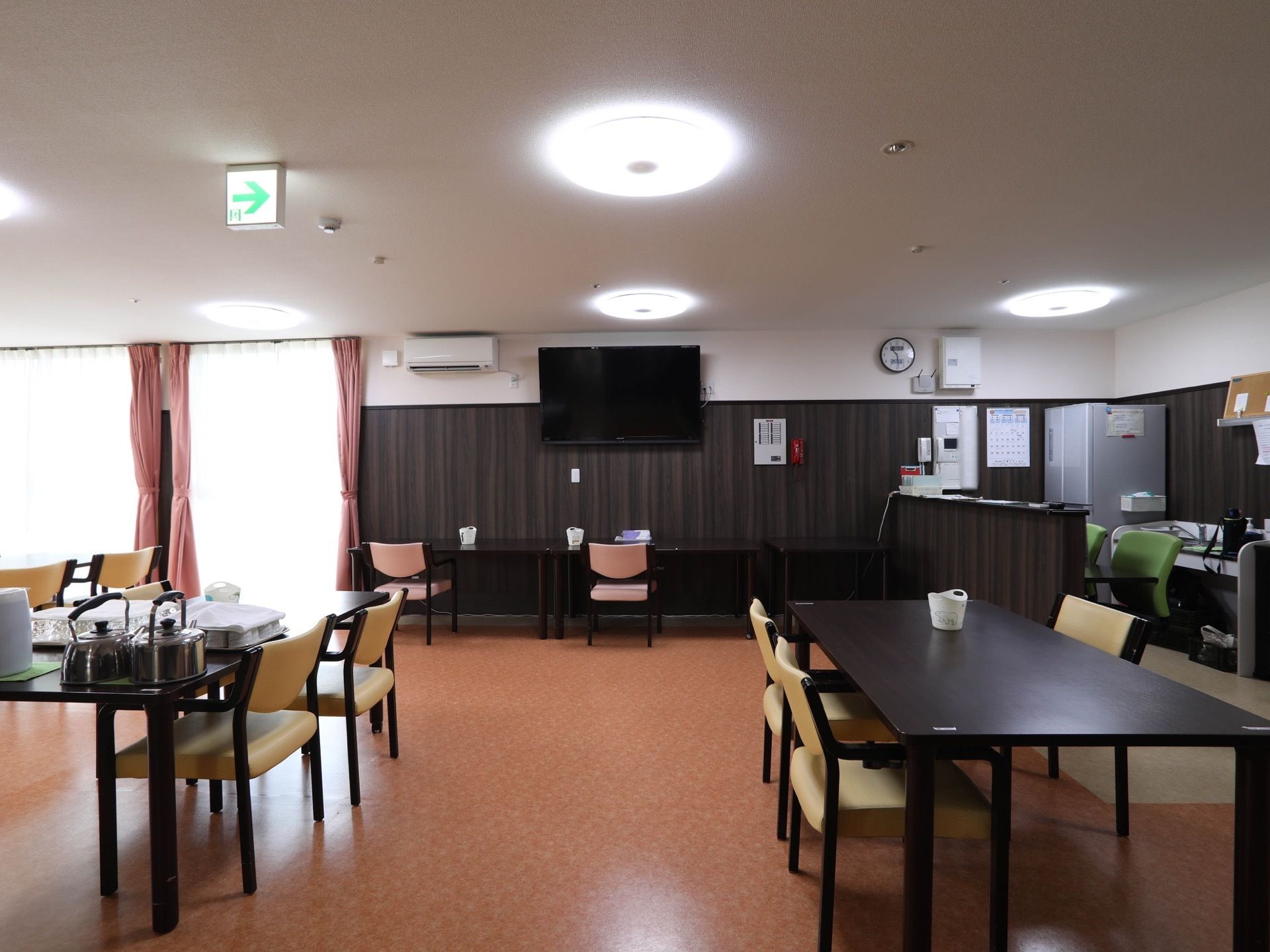壁掛けテレビの下に壁に向かって座る席が設けられている。手前のテーブルの上にはやかんやコップが並べられている。