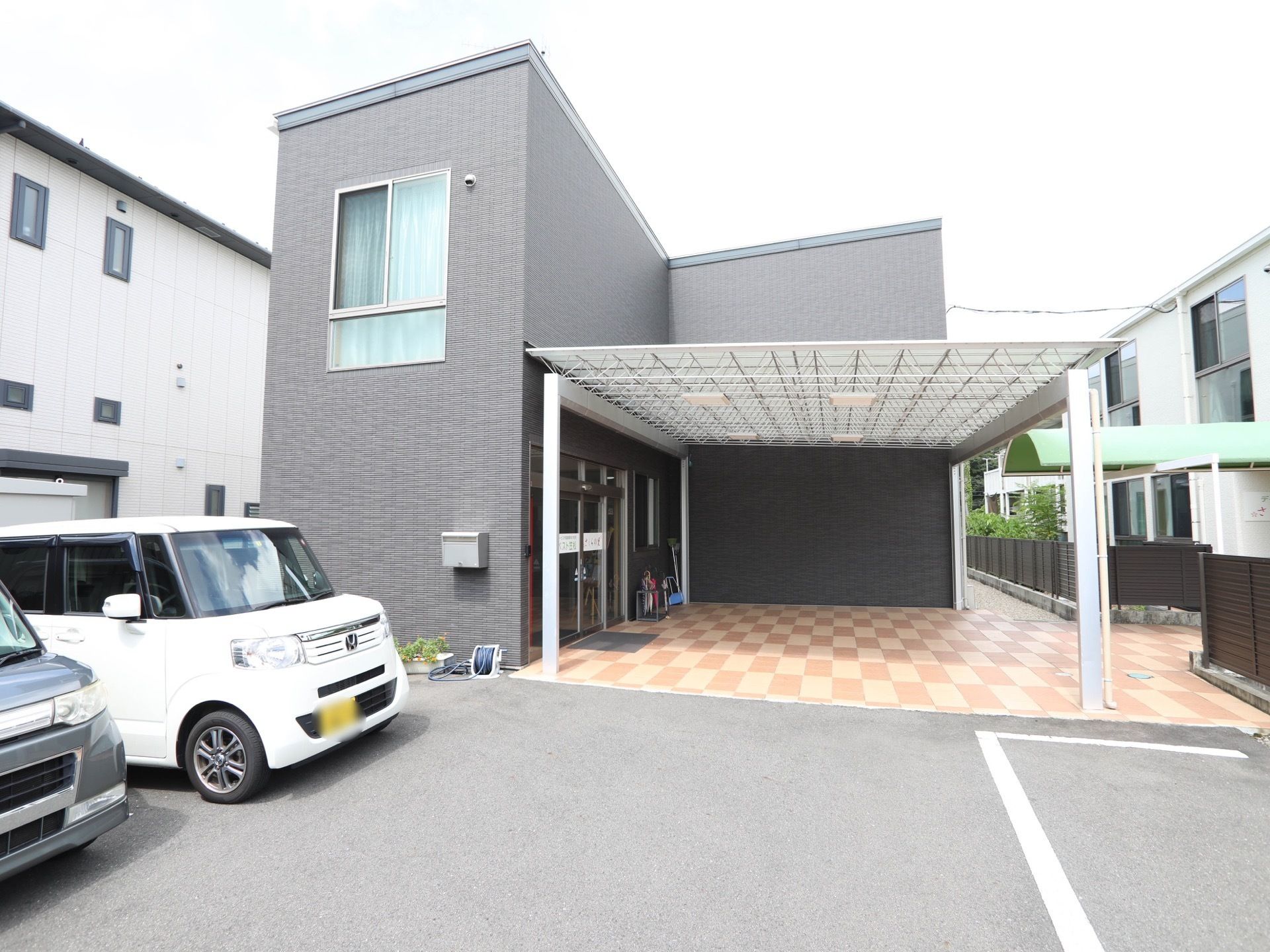 建物の前に駐車スペースがあり、車が停まっている。玄関前には屋根がついており、ドアの横には傘立てがある。