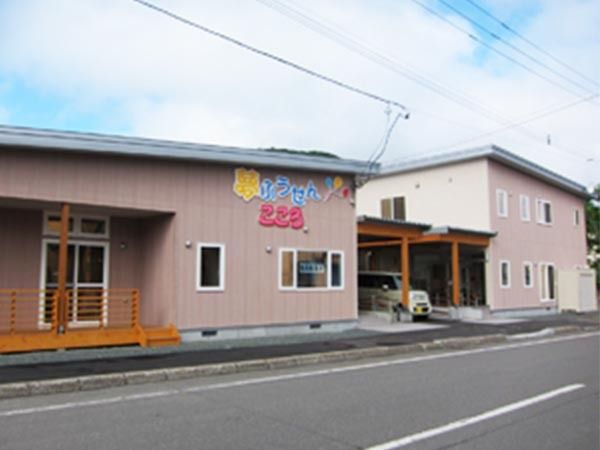 2階建ての建物。外壁にはホーム名と風船のイラストが描かれ、駐車スペースには白い車が止まっている。