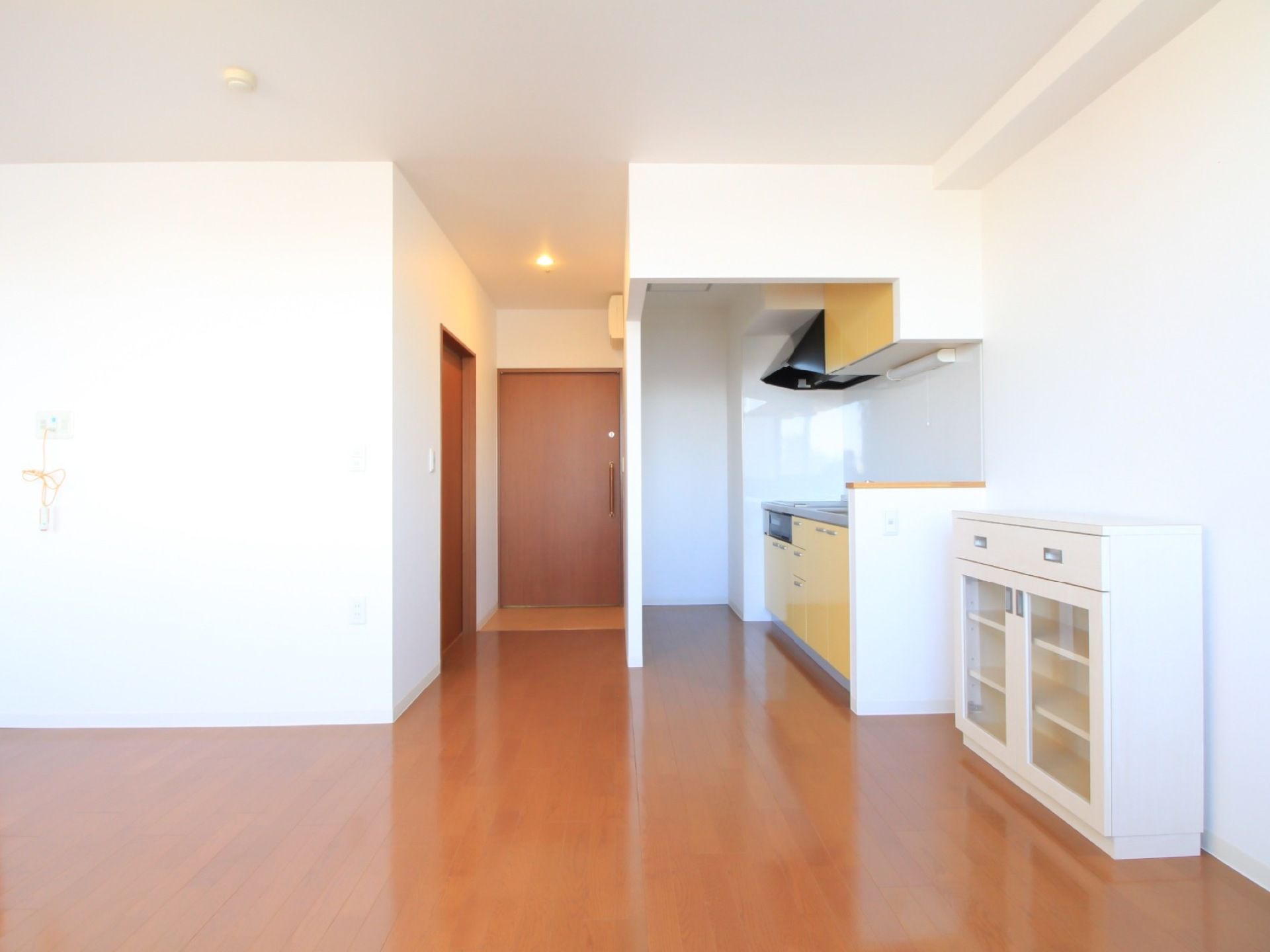 広々とした居室である。収納棚、キッチンが完備されている。壁は白く、部屋全体が明るい。床はフローリングである。