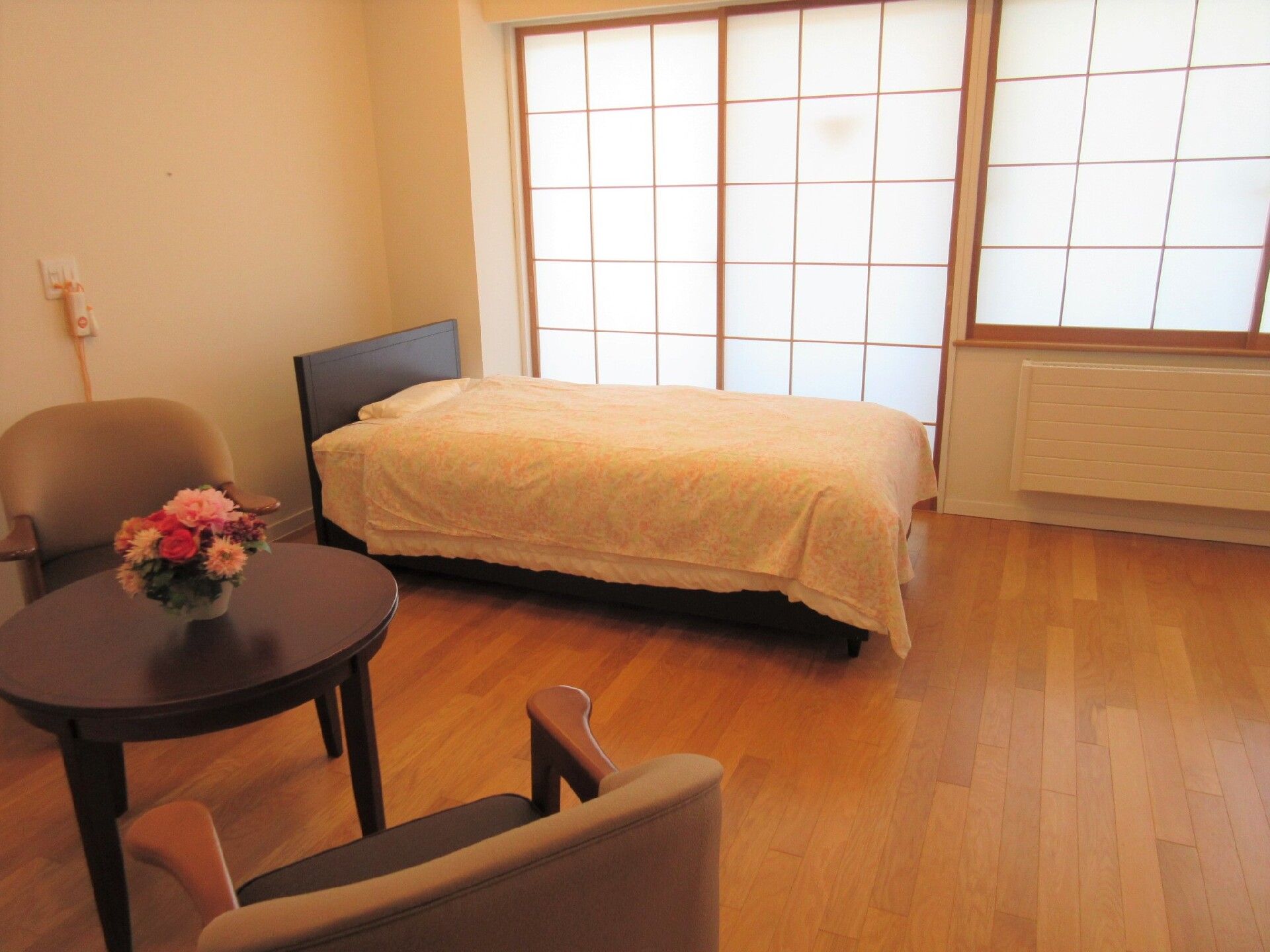 椅子二つとお花が乗った丸テーブル、ベッドが配置された部屋