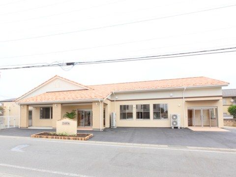 通りに面して建つ、明るい色調の外壁や屋根を持つ平屋建ての施設