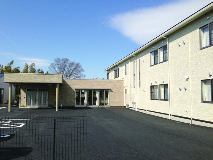広めの敷地内に駐車場スペースと建物が建っている様子。オールバリアフリーのエントランスが写っている写真
