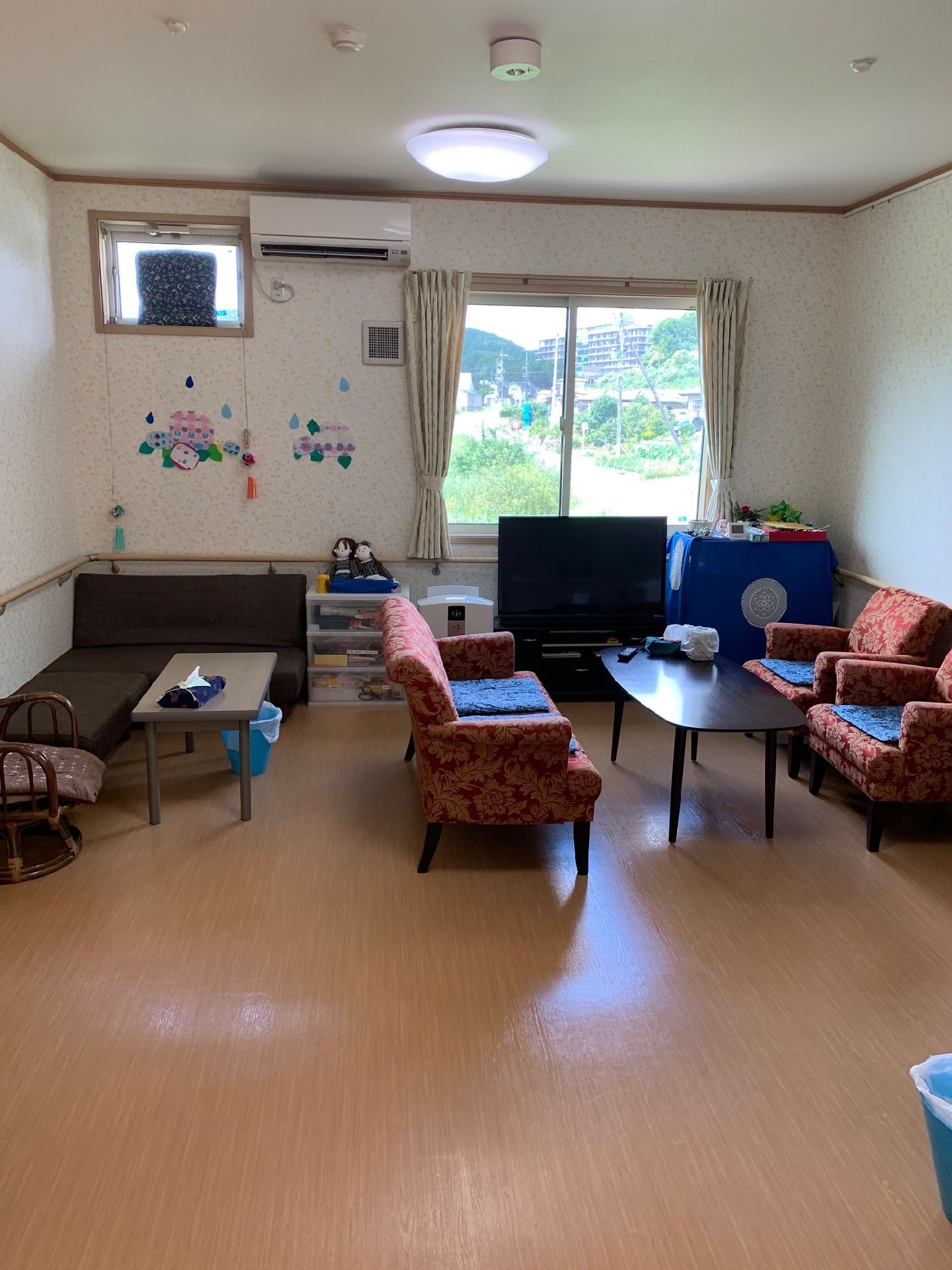 ブルーのエプロンを付けた若い女性スタッフが車いすの高齢女性のそばに寄り添い、笑顔で屋外で過ごしている。