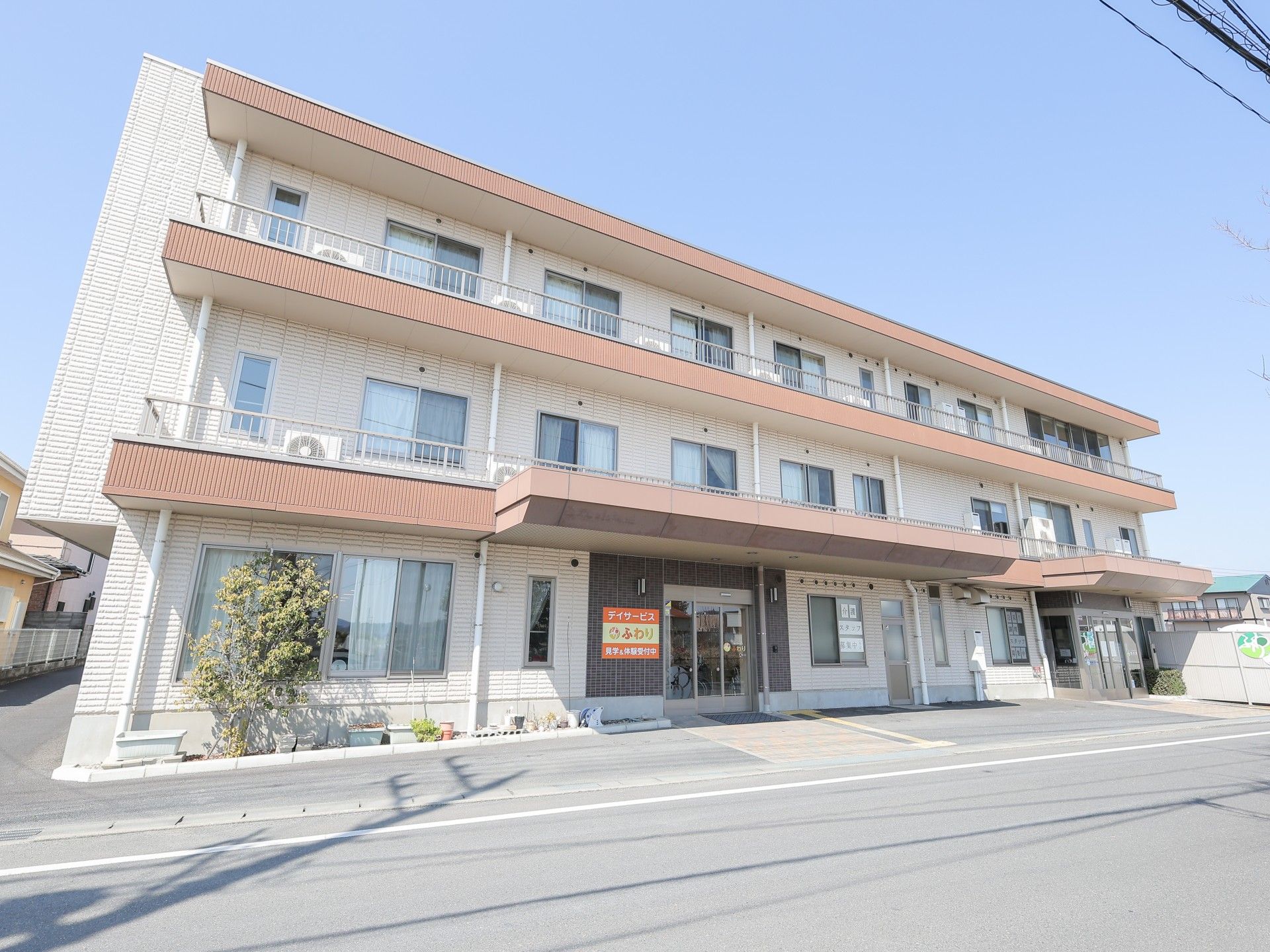 ベージュとブラウンの２階建ての建物は日当たり良好。外壁には住宅名が書かれている。