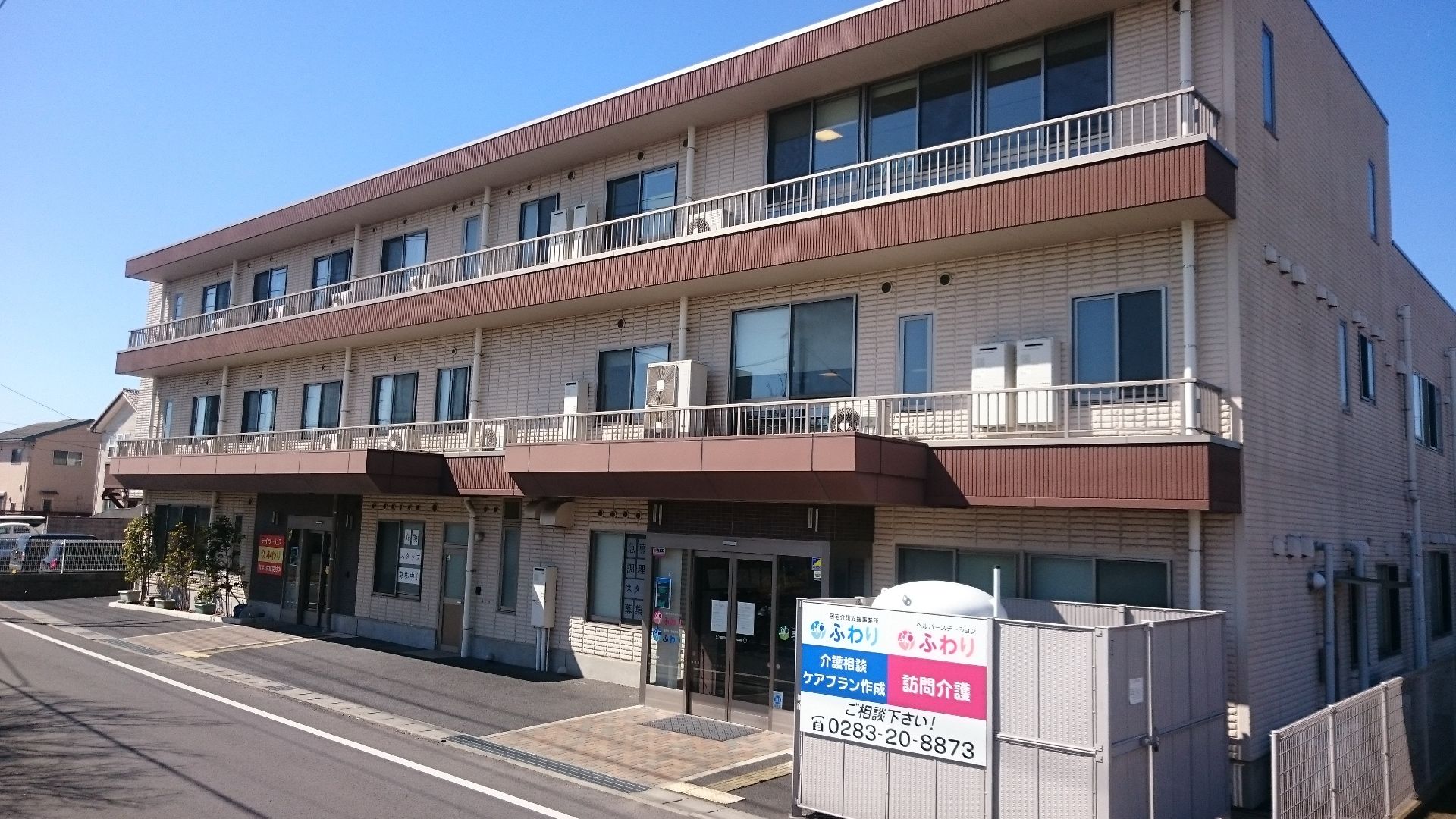 ブラウン系の外壁の２階建ての建物の玄関には自動ドアが設置され、館銘板が建っている。