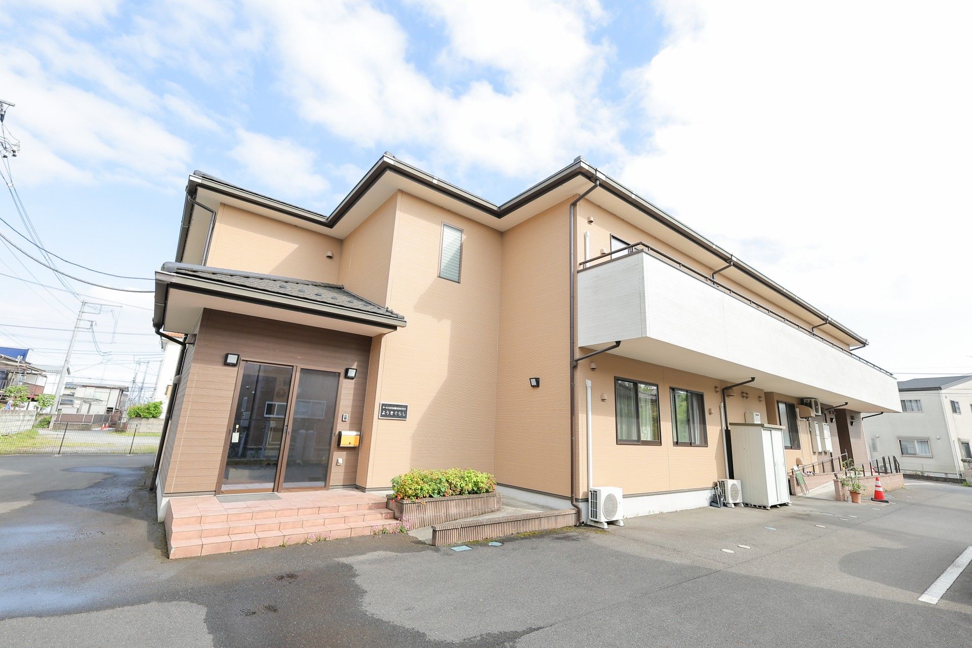 こちらを向いて笑顔になる車いすの高齢女性と介護施設の女性スタッフの様子