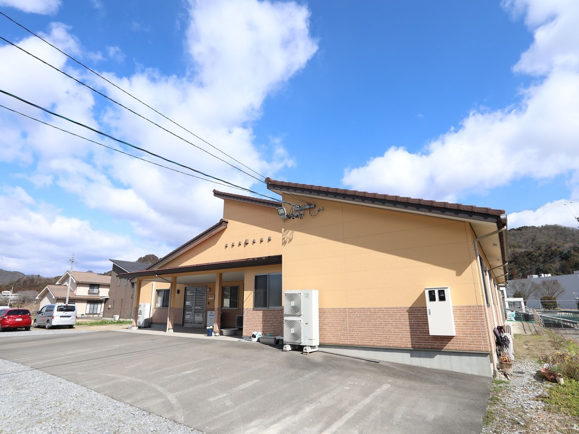 施設は斜めになった屋根が印象的な、1階建ての建物である。建物の前には広いスペースがあり、まわりには家や山などが見える。