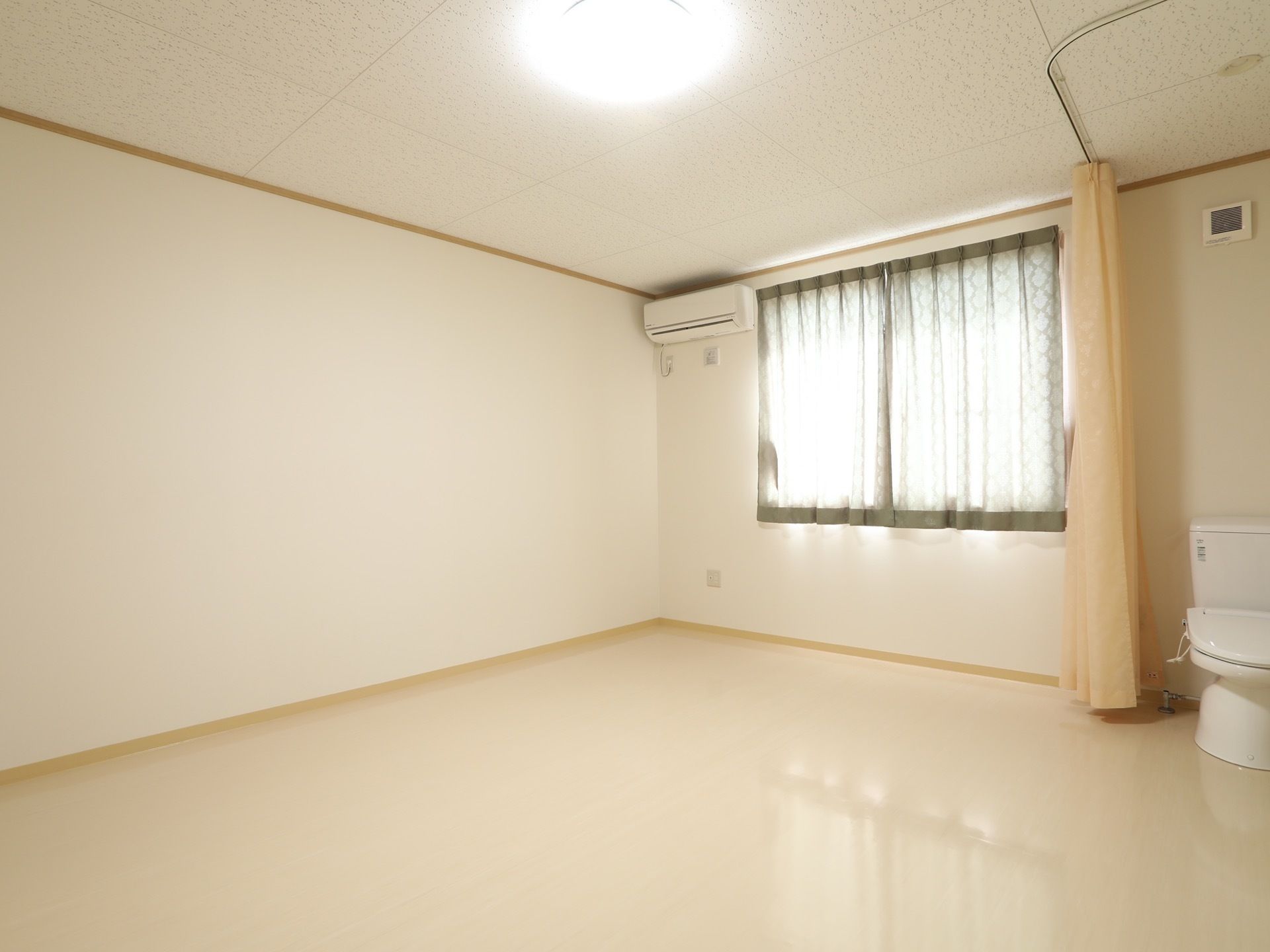 白い内装で明るく、広々とした居室である。右側にはトイレが設置されており、カーテンで仕切られるようになっている。