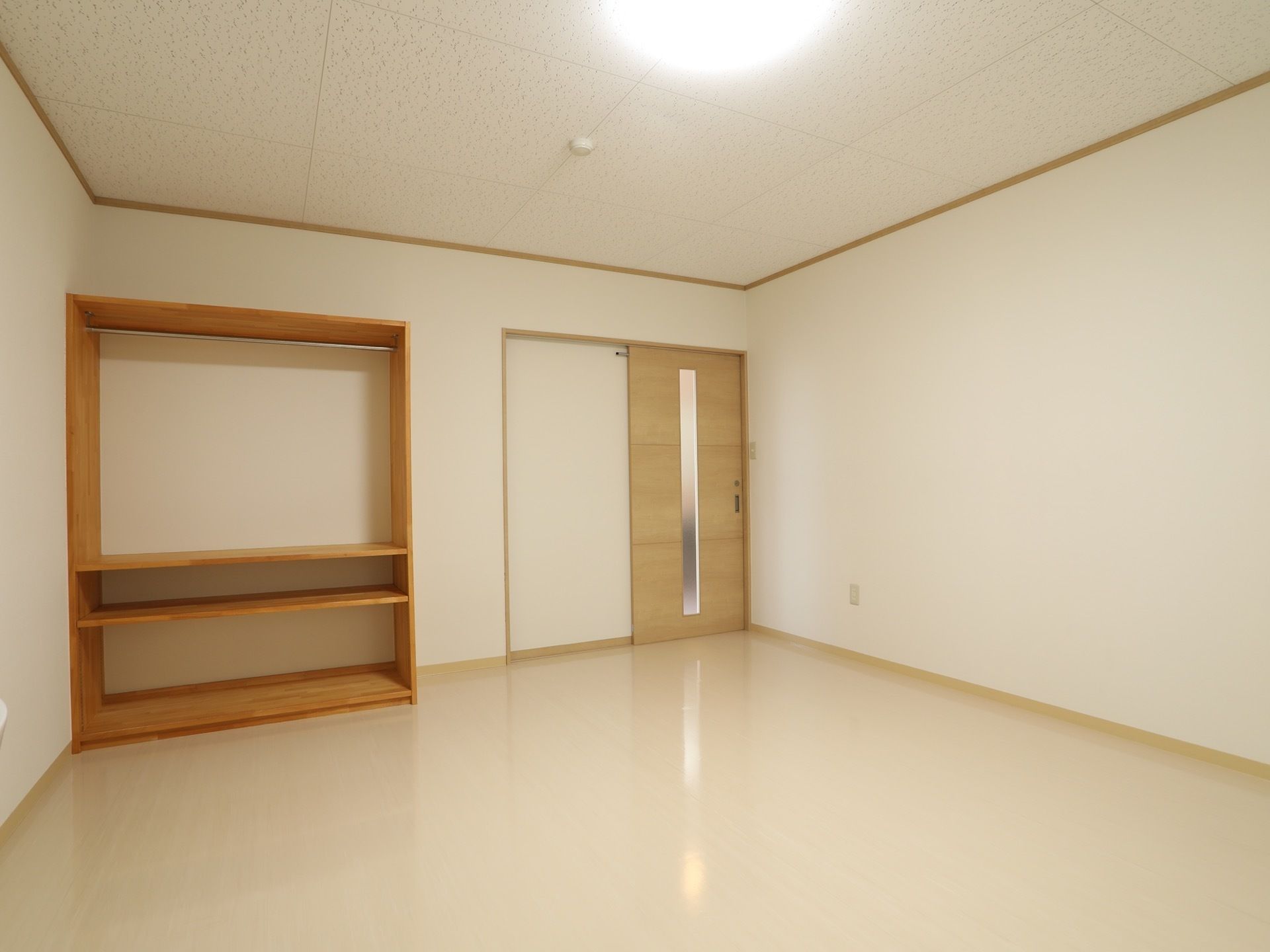 居室は広々としていて、ドアは木目調の引き戸が設置されている。ドアの左側には木製の大きな収納が備え付けられている。