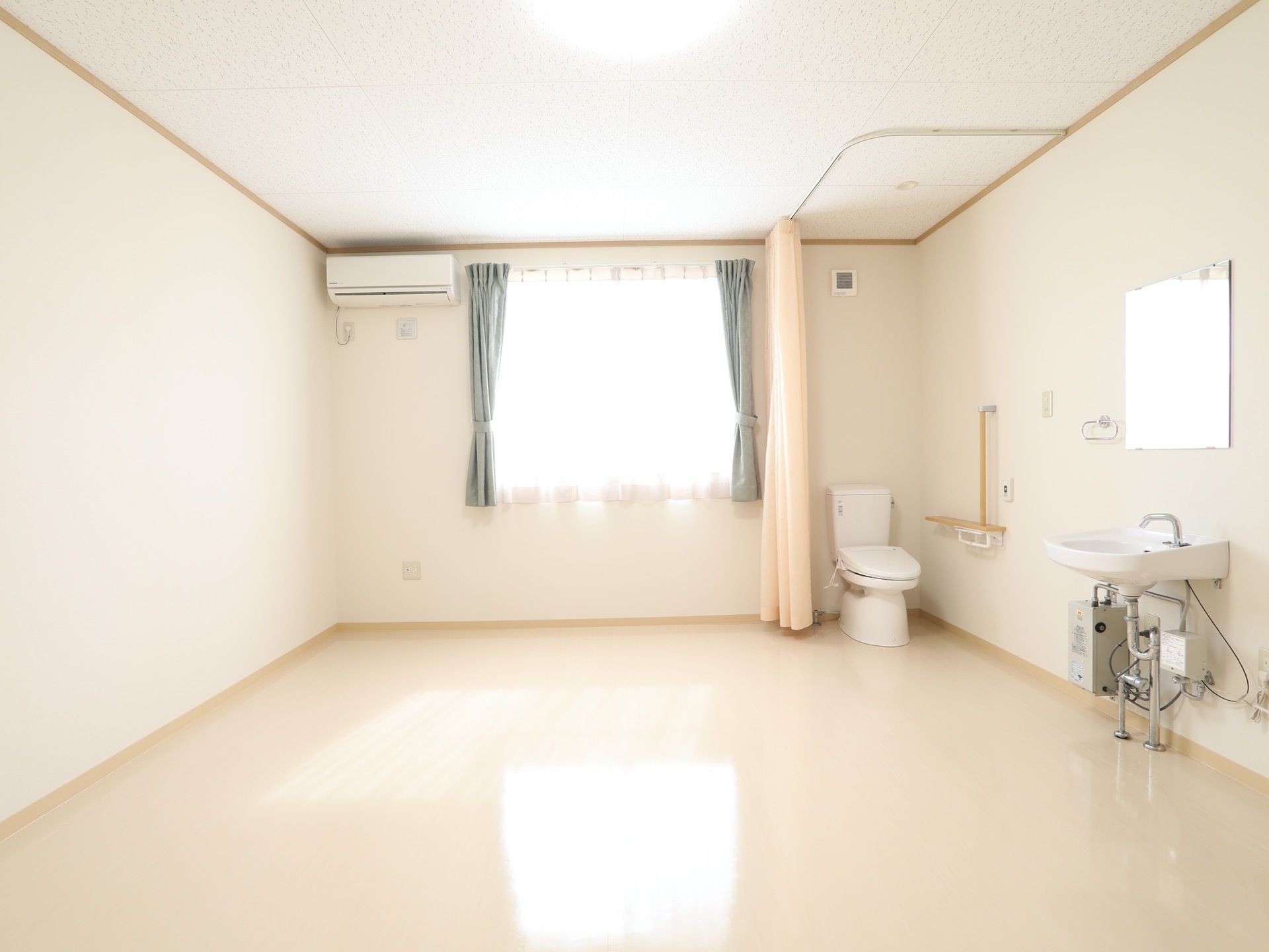 広々とした明るい空間の居室である。右側の壁には洗面台が備えられており、奥の方にはトイレが設置されている。