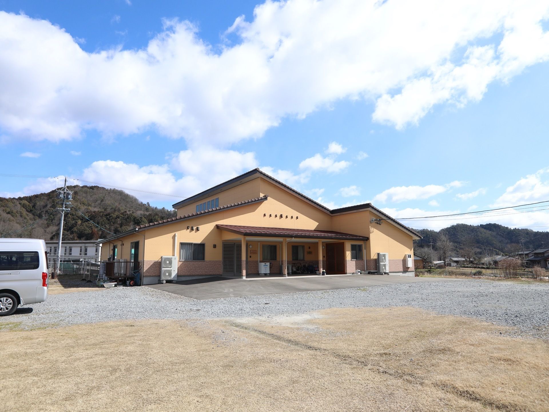 施設は薄いオレンジ色の外壁になっていて、斜めの屋根が付いている。建物の前は広いスペースがあり、左側に車が1台停まっている。