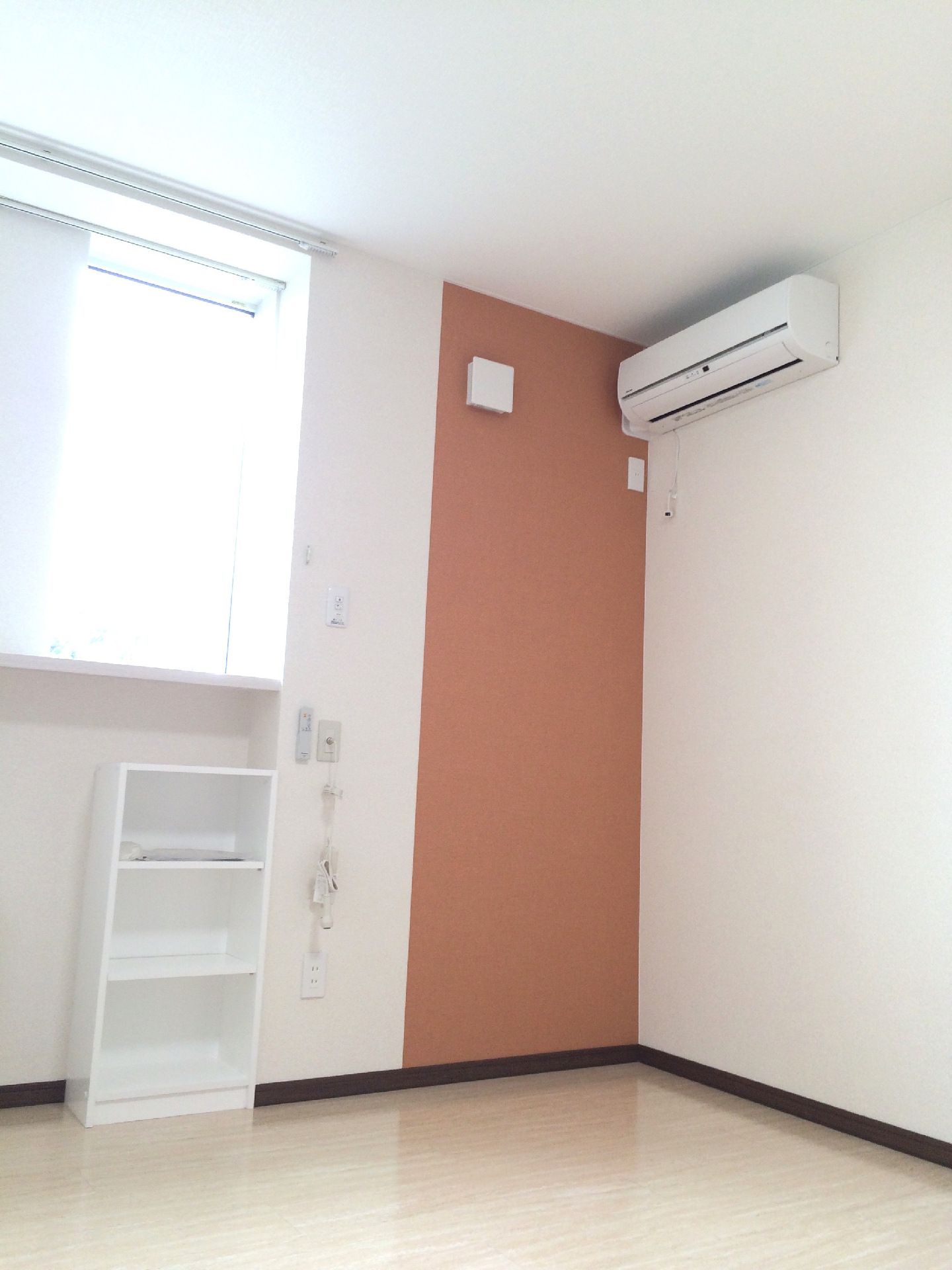 エアコンが付いたフローリングの部屋には白い棚が付いていて、窓もあり明るい雰囲気。壁にはエンジのアクセントクロスや花のイラストがある。