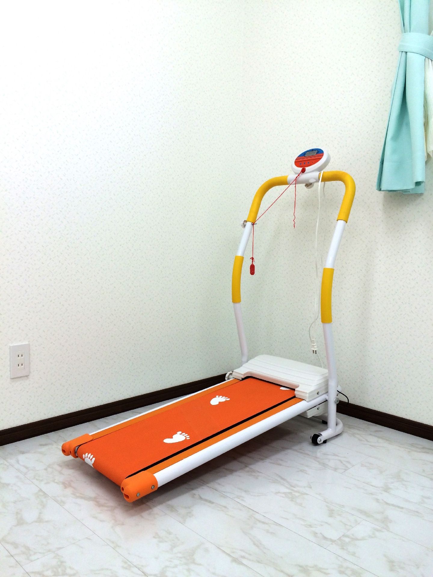 窓のそばにあるウォーキングマシン。オレンジと黄色、白でまとめられていてオレンジのベルトには白い足跡のイラストが描かれている。