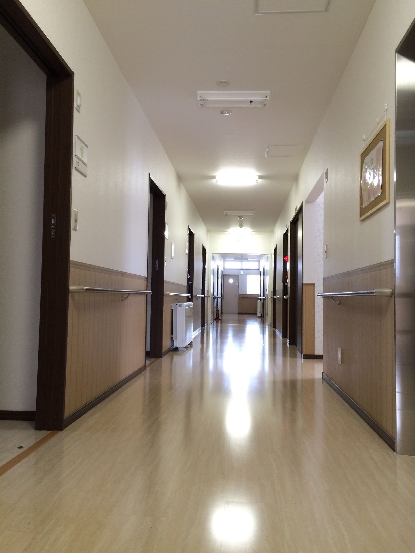 幅の広い廊下はまっすぐで、手すりが両サイドにつき、突き当りには窓がある。居室のドアは引き戸で、廊下の両サイドにある。