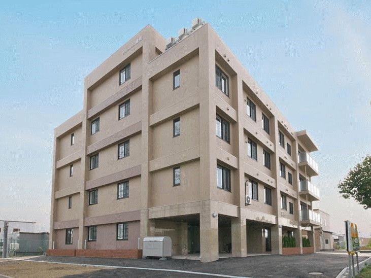 鉄骨造の背の高い建物の様子。マンション風の外観、駐車場スペースが写っている写真