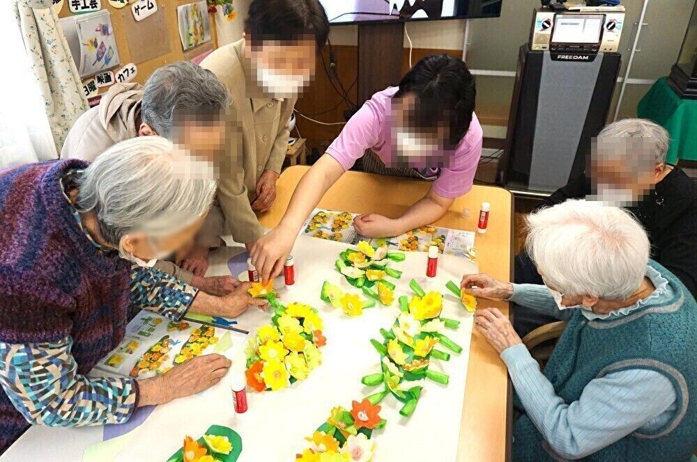 敷地の入り口の側に小さな花がたくさん咲いている、2階建ての施設の外観