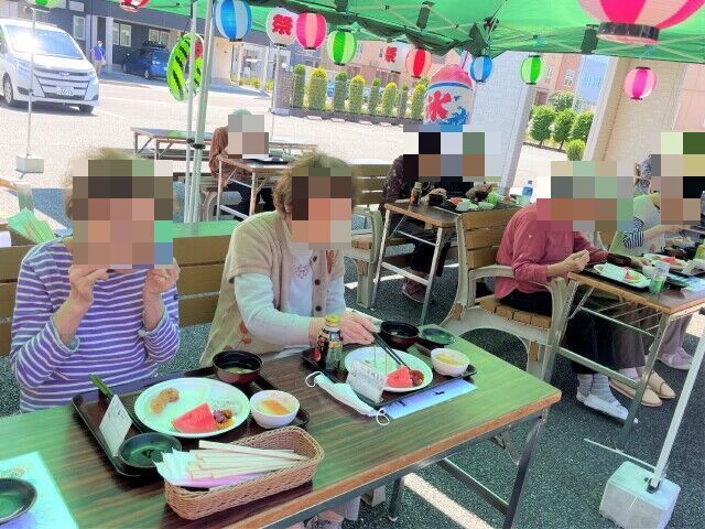 外出イベントでひまわり畑に出かけている様子。車いすの人、その後ろに立って微笑む人々