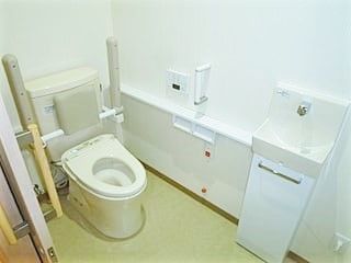 立ち上がり用の可動式手すりが付いた高齢者施設のトイレの写真